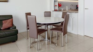 A modern dining area with a round table and six chairs, a green sofa with a brown cushion, a kitchen with white cabinets, and a pendant light above the table. - 3 bedroom accommodation in Sint Idesbald (Sint Idesbald)