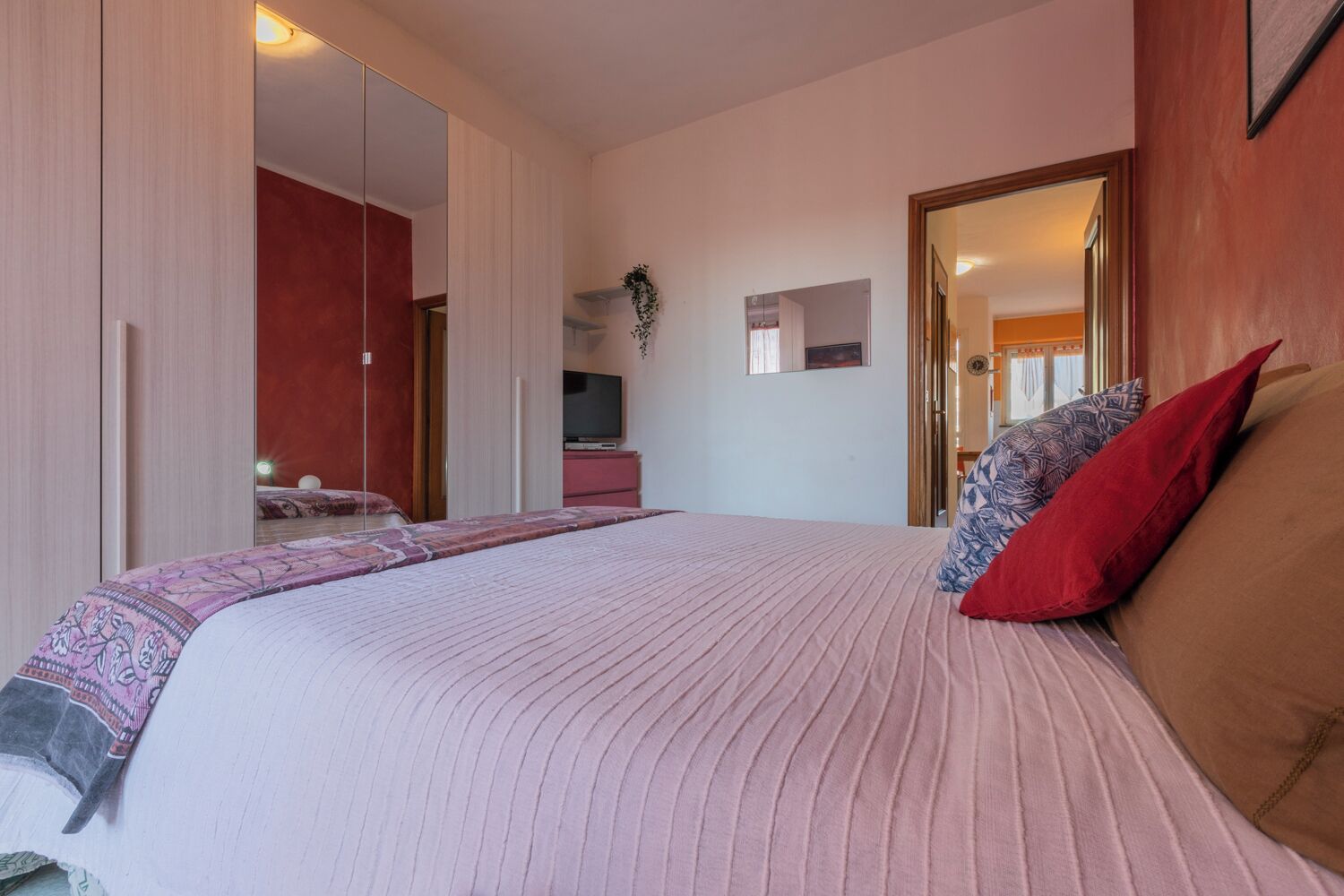 A bedroom with a large bed, a TV, a wardrobe, and a mirror.
