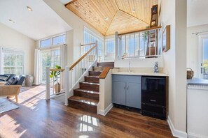 Un ampio soggiorno con scala in legno, cucina con lavastoviglie e ampie finestre che permettono l'ingresso di luce naturale.