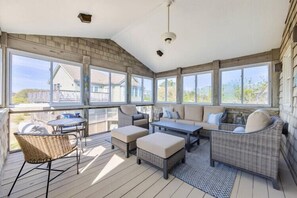 A covered patio with wicker furniture, large windows, and a view of the neighborhood. - Updated Home, Very Close to the Beach! (Duck)