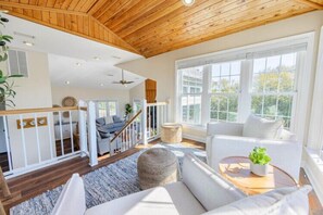 Amplia sala de estar con techo de madera, una escalera y un gran ventanal con vistas al exterior.