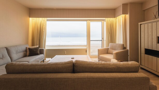 Quarto de hotel com uma janela grande, um sofá, uma cadeira e um armário.