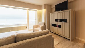 Sala de estar moderna com uma janela grande, sofá, poltrona, televisão sobre um móvel e vista para o mar.