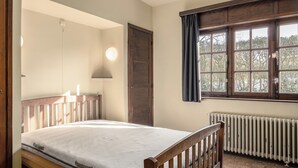 Un dormitorio con cama de madera, ventana con cortinas, un radiador y una puerta.