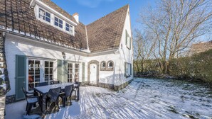 Un edificio blanco con techo de tejas, un patio con mesas al aire libre y suelo cubierto de nieve.