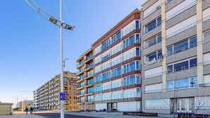 A multi-story residential building with balconies, a pedestrian walkway, and a clear sky.