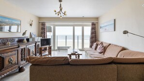 A living room with a sofa, TV, and a view of the beach.