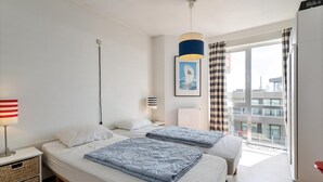 Hotelkamer met twee bedden, een nachtkastje met lamp, een lijst met afbeelding aan de muur, en een raam met gordijnen.