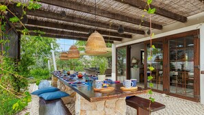 An outdoor dining area with a stone island, wooden benches, and hanging wicker lamps. - Casa Dos Amigos in S o Bartolomeu de Messines (Silves)