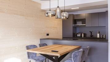 A modern kitchen with a wooden island, grey chairs, and pendant lighting.