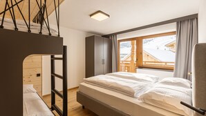 Ein Schlafzimmer mit Etagenbett, einer Holzleiter, einem Kleiderschrank und einem Fenster mit Blick auf eine verschneite Landschaft.