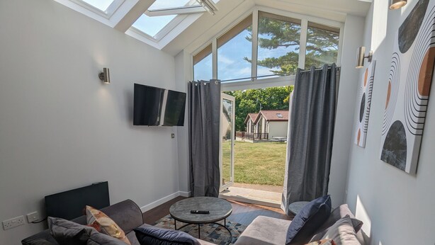 A modern living room with a sofa, a coffee table, and a TV mounted on the wall. - Cozy Two Bedroom Chalet in Sidmouth (Sidmouth)