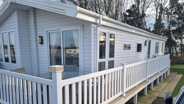 Une maison mobile blanche dotée d’une terrasse couverte et d’un porche clôturé.
