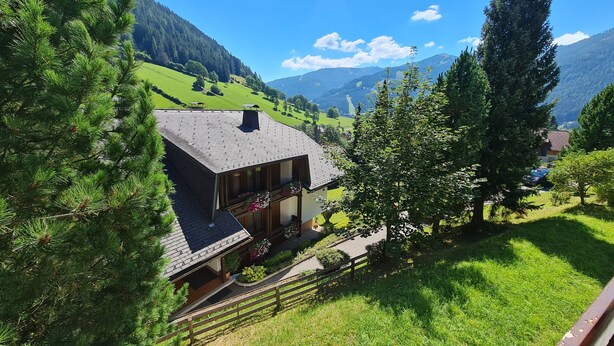 Una casa con techo inclinado, una terraza de madera y vistas a un valle verde y montañas.