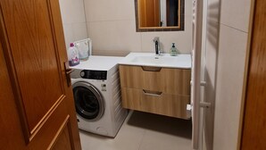 Un baño pequeño con lavadora, lavabo y espejo.