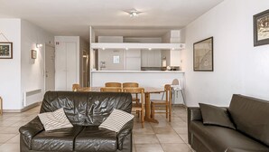 A modern living room with a leather sofa, a dining table with chairs, and a kitchen area in the background.