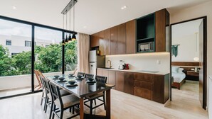 A modern kitchen with wooden cabinets, a dining area with a glass table, and a view of greenery outside. - Luxury Penthouse│Private Rooftop Pool│Concierge (Tulum)