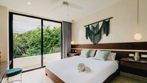 A modern hotel room with a large bed, a sitting area with a green chair, a ceiling fan, and a view of greenery outside. - Luxury Penthouse│Private Rooftop Pool│Concierge (Tulum)