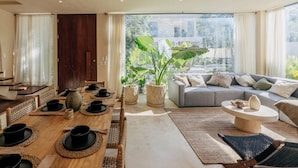 Una sala de estar moderna con comedor, un sofá y un amplio ventanal con vistas a zonas verdes.