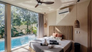 Un dormitorio moderno con una cama grande, un ventilador de techo, un equipo de aire acondicionado, una mesita de noche y vistas a una piscina.
