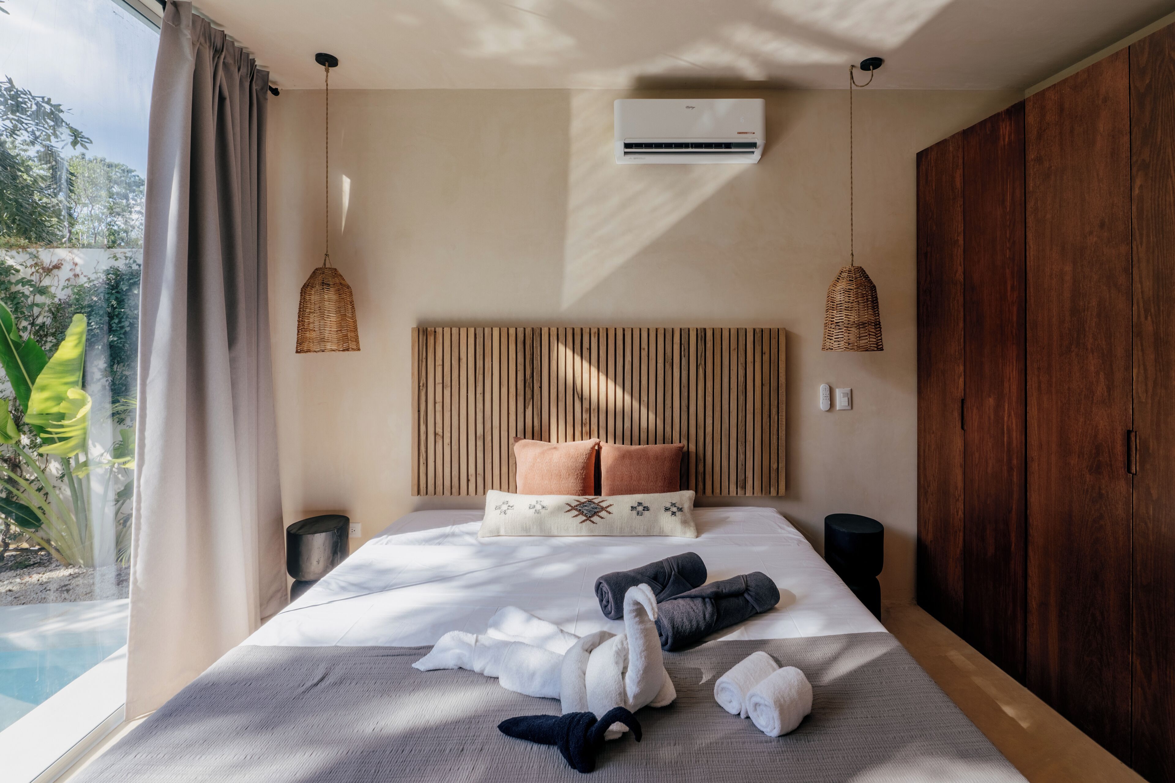 Ein Schlafzimmer mit einem großen Bett, zwei Nachttischen, einer Klimaanlage und Blick auf einen Swimmingpool.