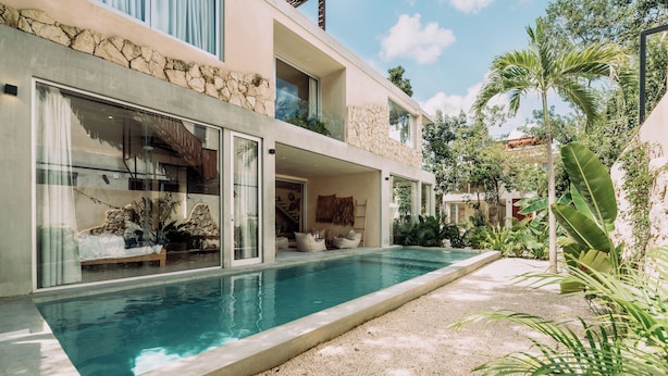 Una casa moderna de dos pisos con piscina, amplios ventanales y fachada de piedra.