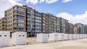 Un edificio residencial de varios pisos con unidades numeradas, cajas eléctricas exteriores y un cielo despejado.
