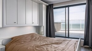 Un dormitorio con cama, ventana con vista al mar y puerta corrediza a un balcón.
