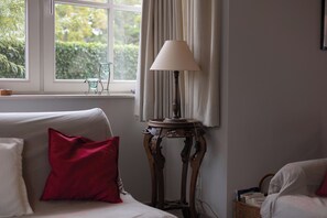 Ein Zimmer mit einem weißen Sofa, einem roten Kissen, einer Tischlampe und einem Fenster mit Vorhängen.