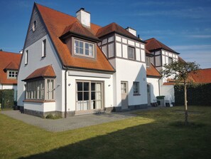 Ein zweistöckiges Haus mit geneigtem Dach, großen Fenstern und einer Haustür.