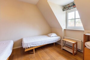 A small, single-bed room with a sloped ceiling, a window with a view of buildings, and a radiator.
