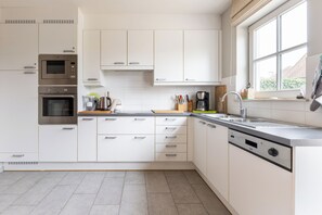 Een moderne keuken met witte kastjes, roestvrijstalen apparatuur, een inbouwvaatwasser en een raam dat voor natuurlijk licht zorgt.