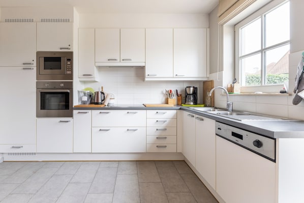 A modern kitchen with white cabinetry, stainless steel appliances, a built-in dishwasher, and a window providing natural light.