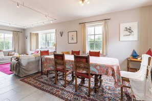 Een ruime kamer met een grote eettafel, meerdere stoelen, een bank en een bed.