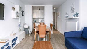A modern living room with a dining area, featuring a blue sofa, wooden dining table, and chairs. - 2 bedroom accommodation in Sint-Idesbald (Sint-Idesbald)