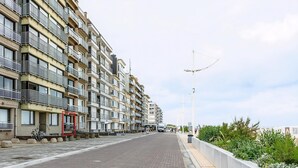 A multi-story residential building with balconies, a red-framed entrance, and a paved walkway. - 2 bedroom accommodation in Sint-Idesbald (Sint-Idesbald)