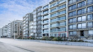 Un immeuble résidentiel moderne à plusieurs étages, doté de balcons, de grandes fenêtres et d’un trottoir dallé.