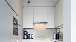 Une cuisine moderne avec des meubles blancs, un four encastré, une machine à café et une bouilloire.