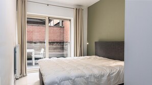 Une chambre avec un lit, une porte-fenêtre coulissante donnant sur un espace extérieur et une chaise à l’extérieur.