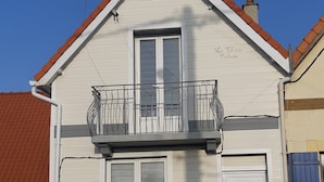 Un edificio de dos pisos con balcón, chimenea y un pequeño porche.
