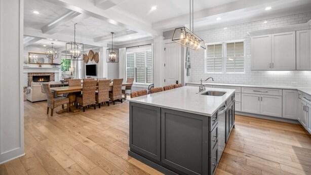 Una cocina moderna con armarios blancos, una isla grande con un lavamanos y una zona de comedor con sillas de mimbre.