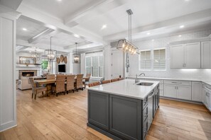 Una cocina moderna con armarios blancos, una isla grande con un lavamanos y una zona de comedor con sillas de mimbre.