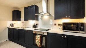 Una cocina moderna con armarios negros, una campana extractora de acero inoxidable, un horno empotrado, un microondas y una cafetera.