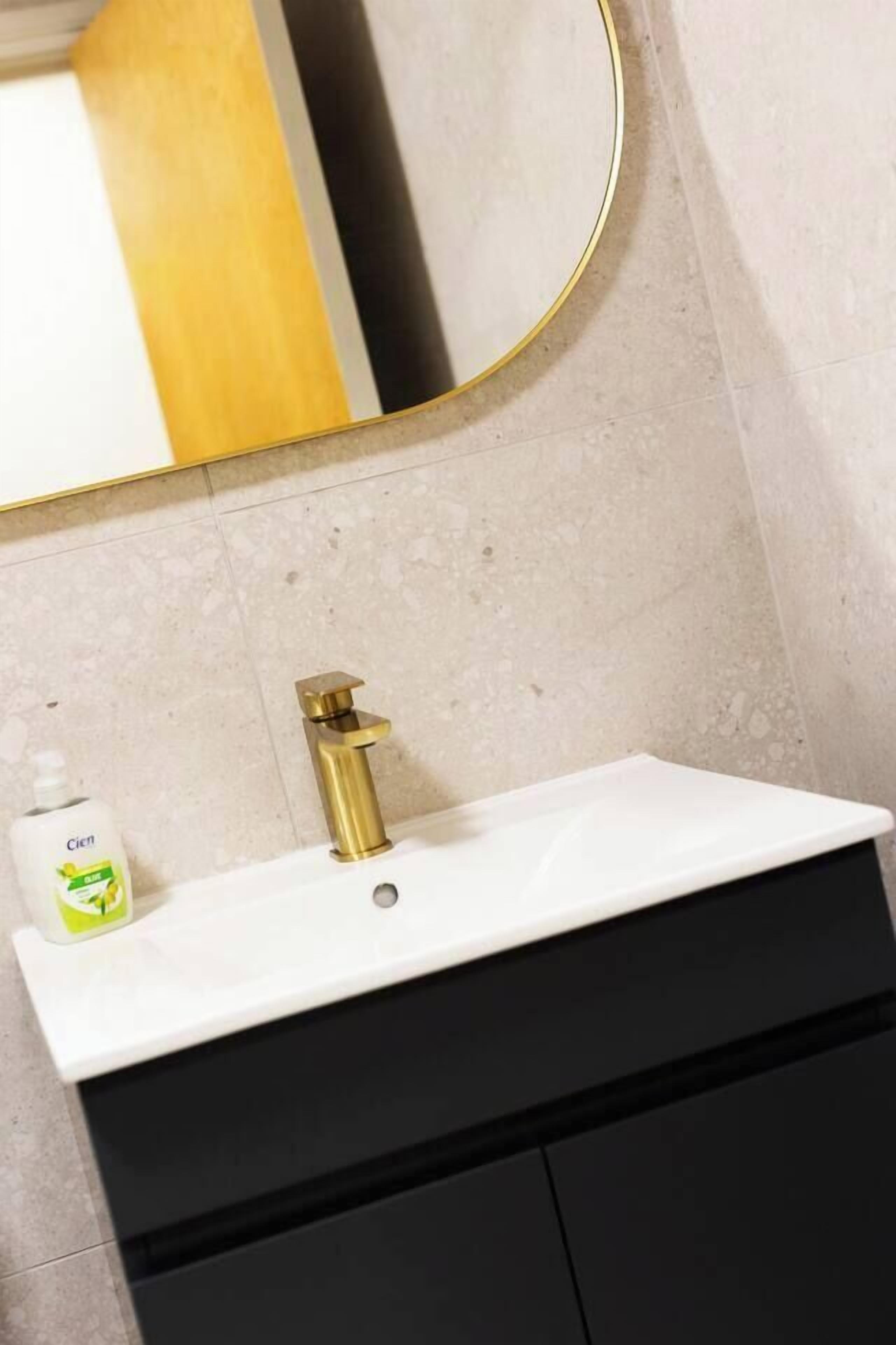 A bathroom with a white sink, a gold faucet, and a mirror with a gold frame.