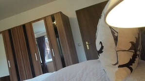Een slaapkamer met een bed, witte kussens, een lamp en een kledingkast.
