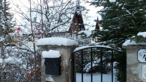 Een sneeuwbedekte poort met een stenen pijler en metalen hekken, leidend naar een gebouw met een traditioneel dak.