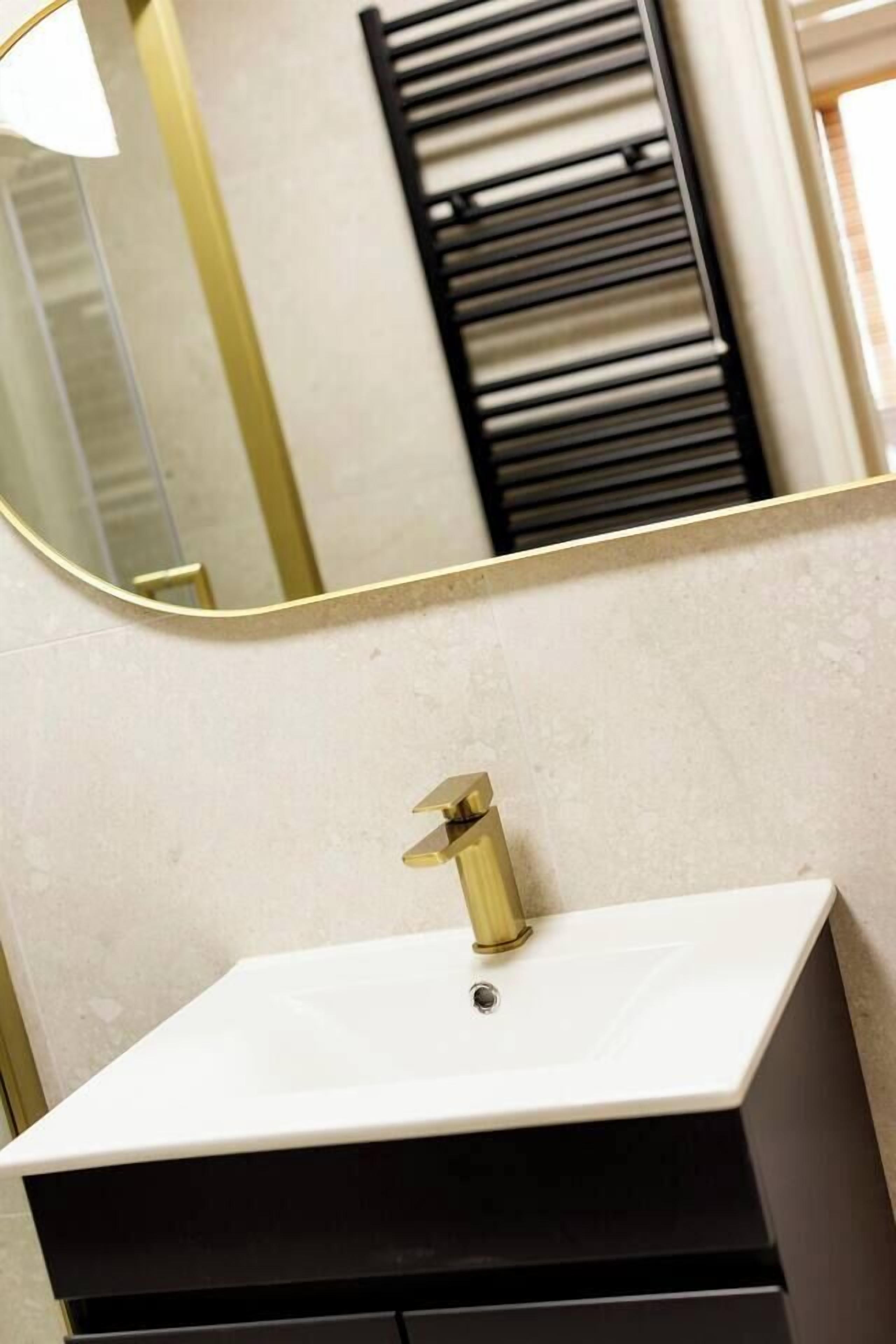 Un baño con un lavamanos blanco, un grifo dorado y un espejo grande con marco dorado.
