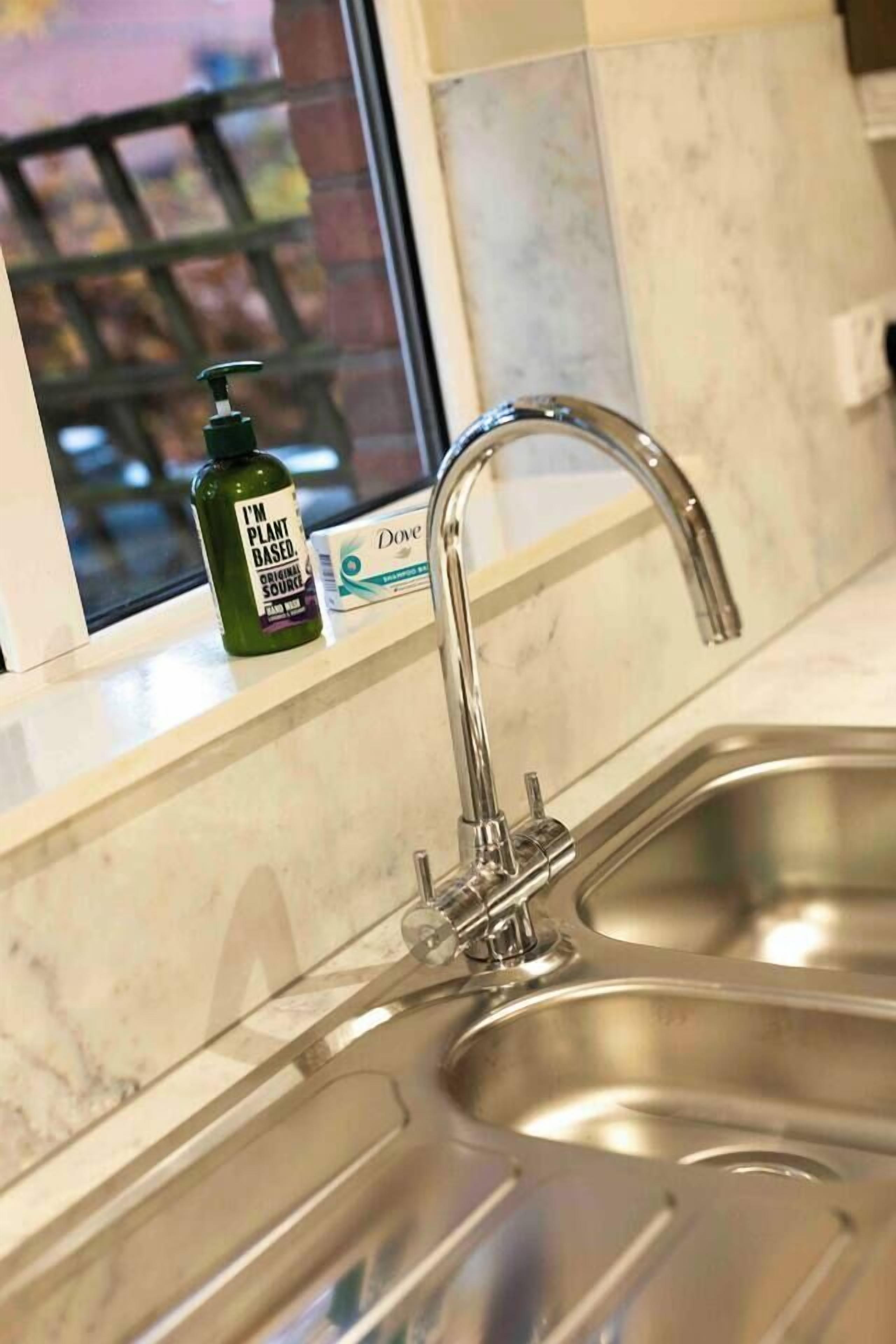 A kitchen sink with a modern faucet, a bottle of Dove soap, and a Dove soap box on the counter.