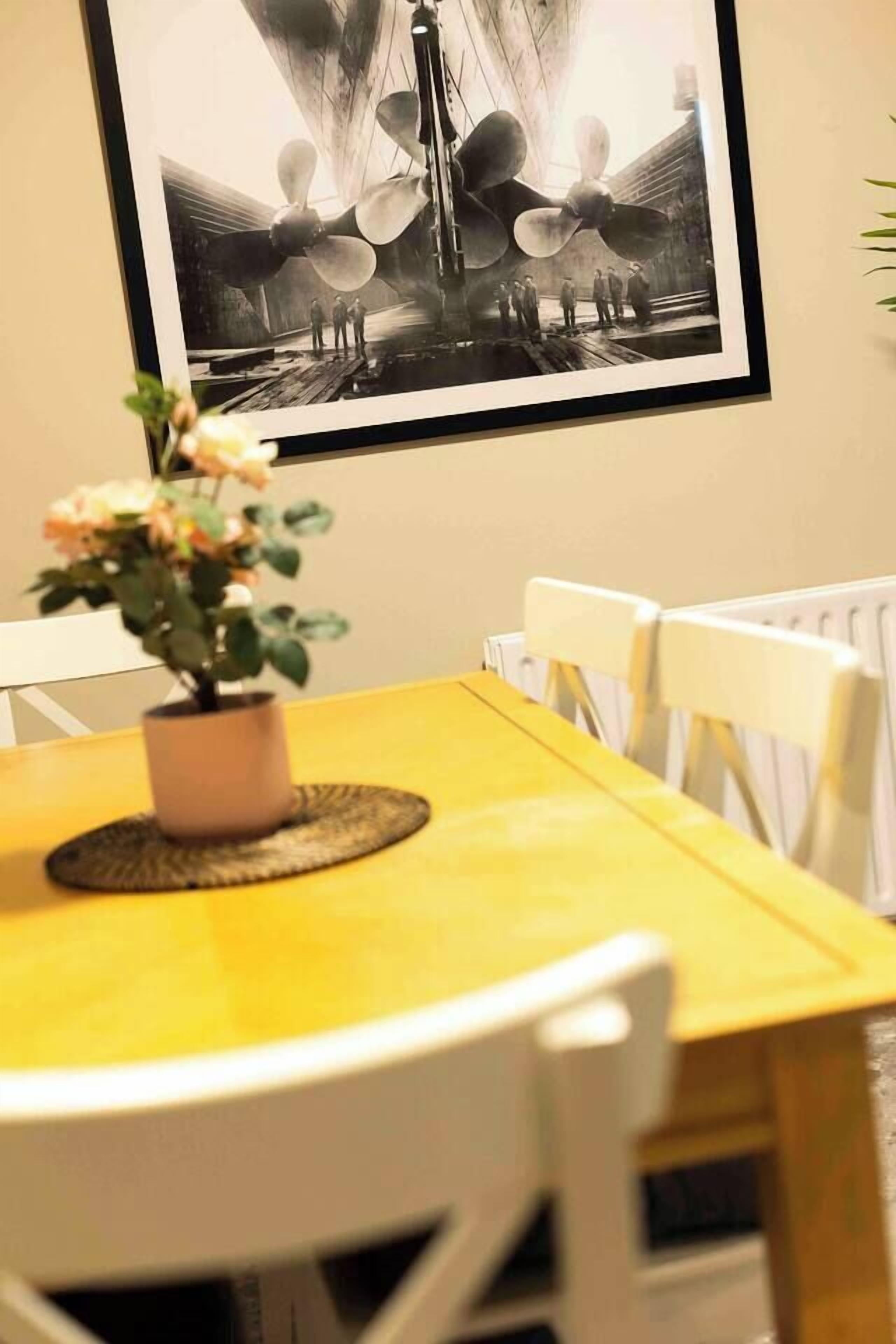 A dining area with a yellow table, white chairs, and a framed black and white photograph on the wall.