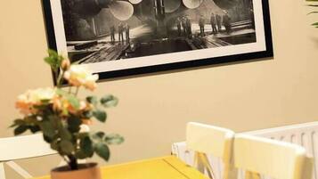 A dining area with a yellow table, white chairs, and a framed black and white photograph on the wall.